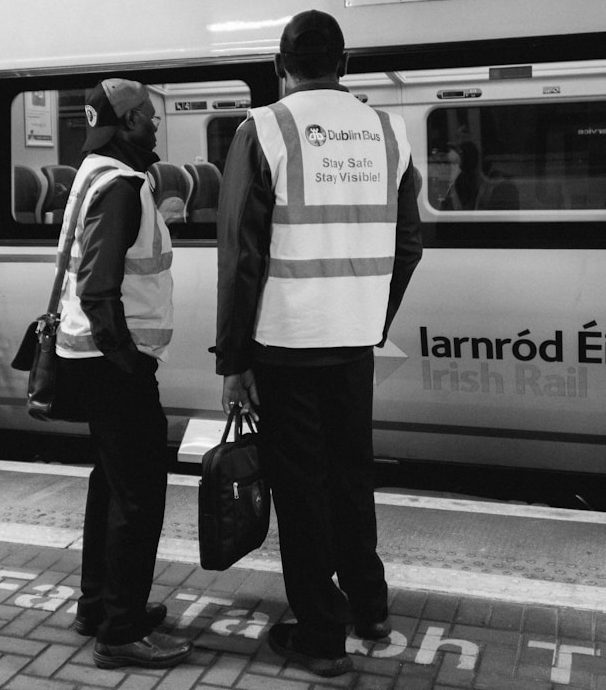Two workers in high-visibility vests talking by a train.