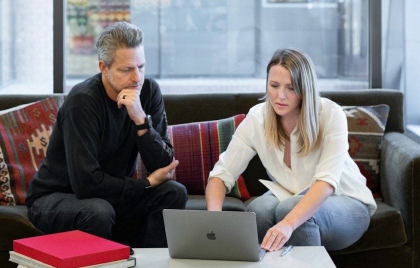 man and woman sitting on couch using macbook