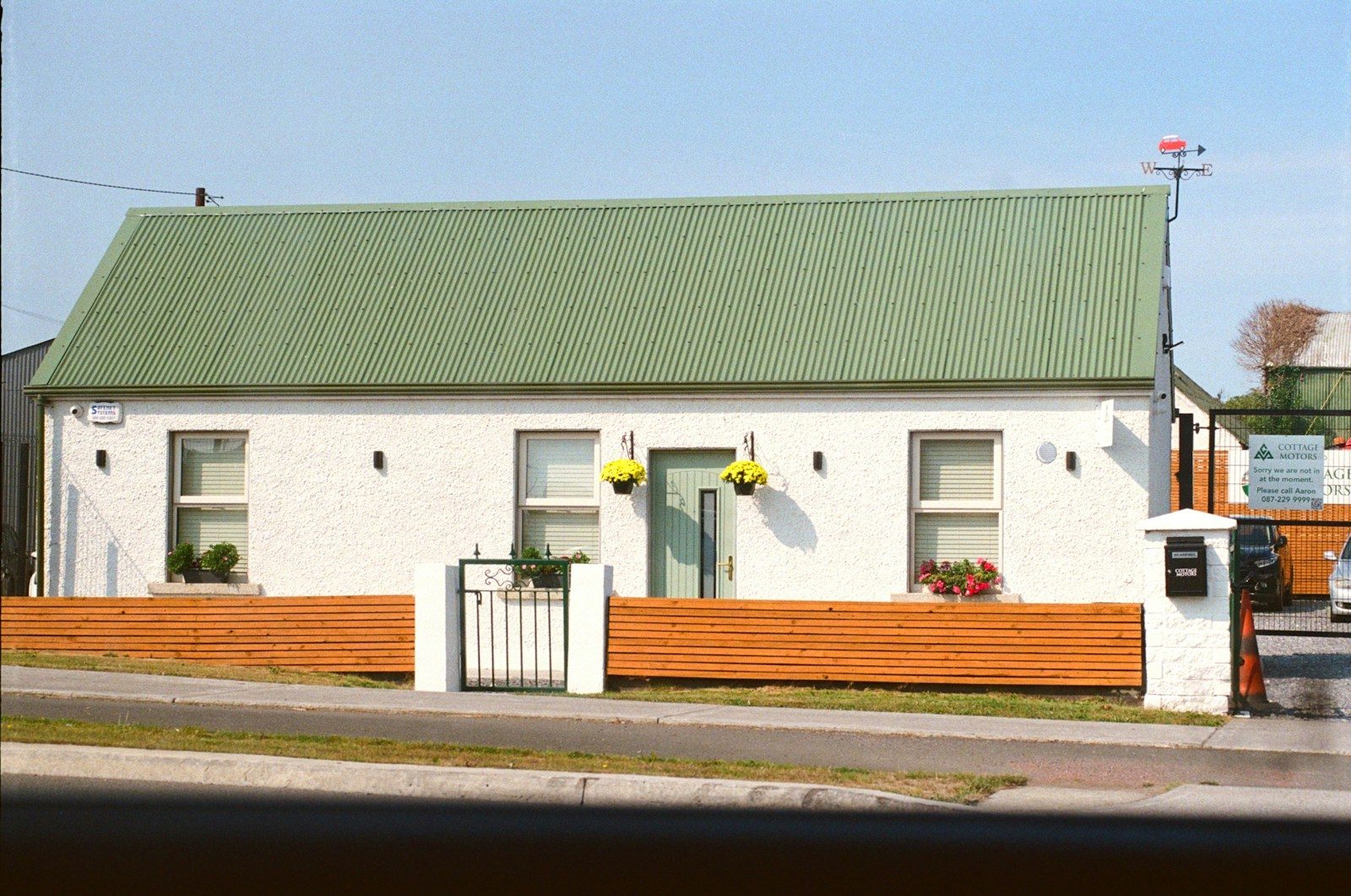 White cottage with green roof and wooden fence